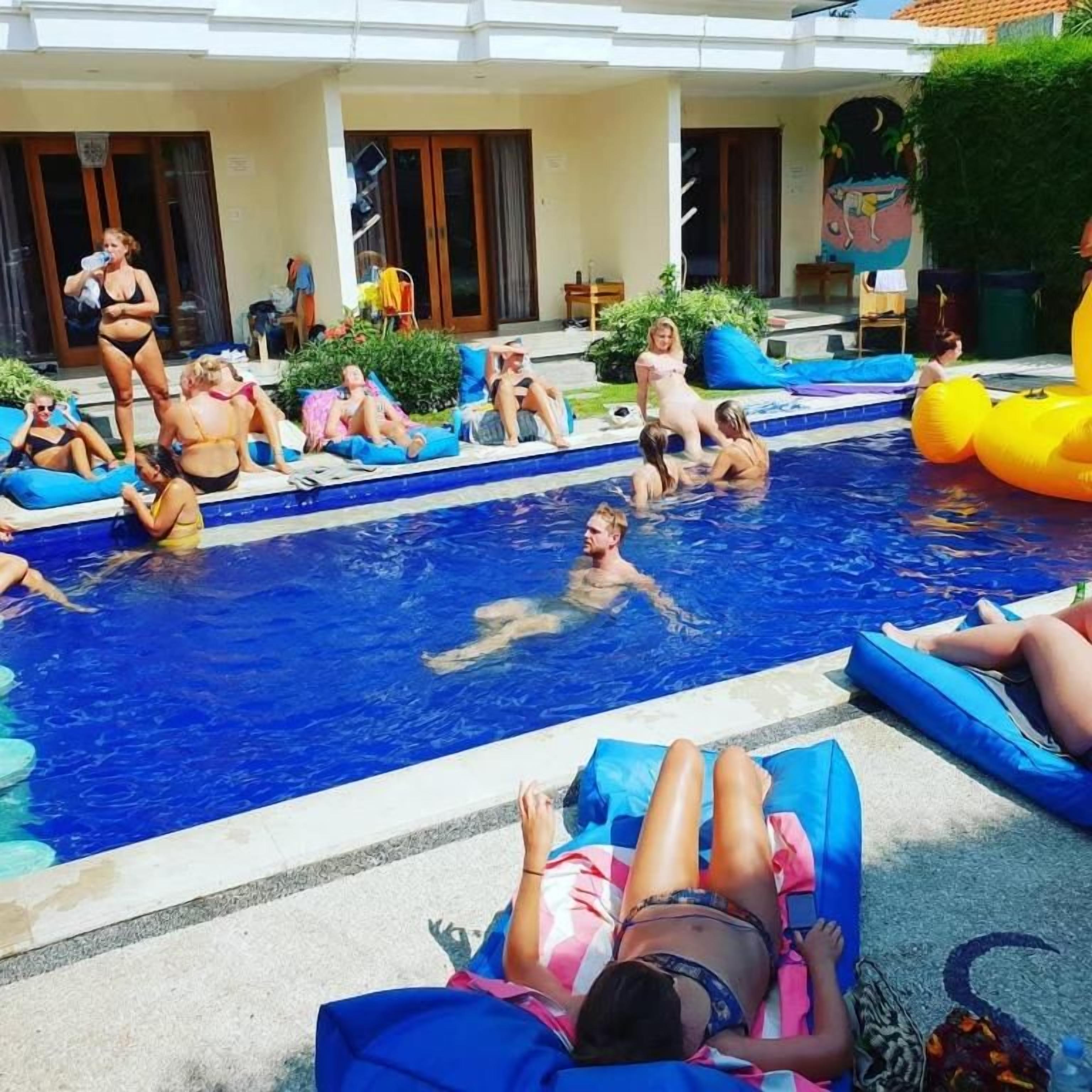 A swimming pool area with people relaxing on lounge chairs and floating devices.
