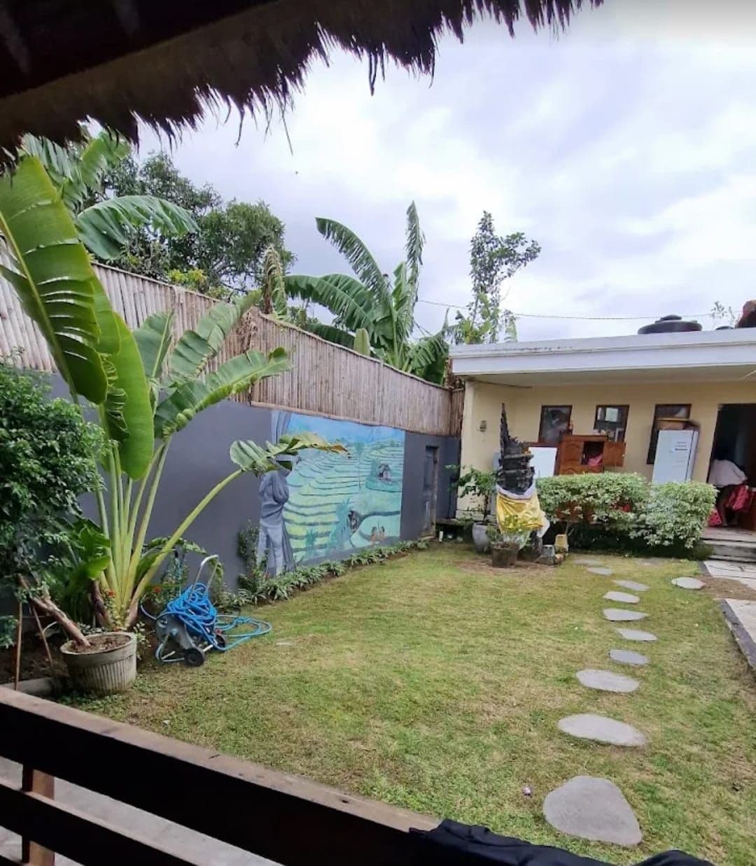 A garden with a mural, a thatched roof structure, and a house with a door and windows.