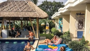 A poolside area with lounge chairs and a bar area. - Castaway Hostel (Badung)