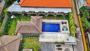 A pool area with a sign reading 'CASTAWAY' and a thatched-roof structure. - Castaway Hostel (Badung)