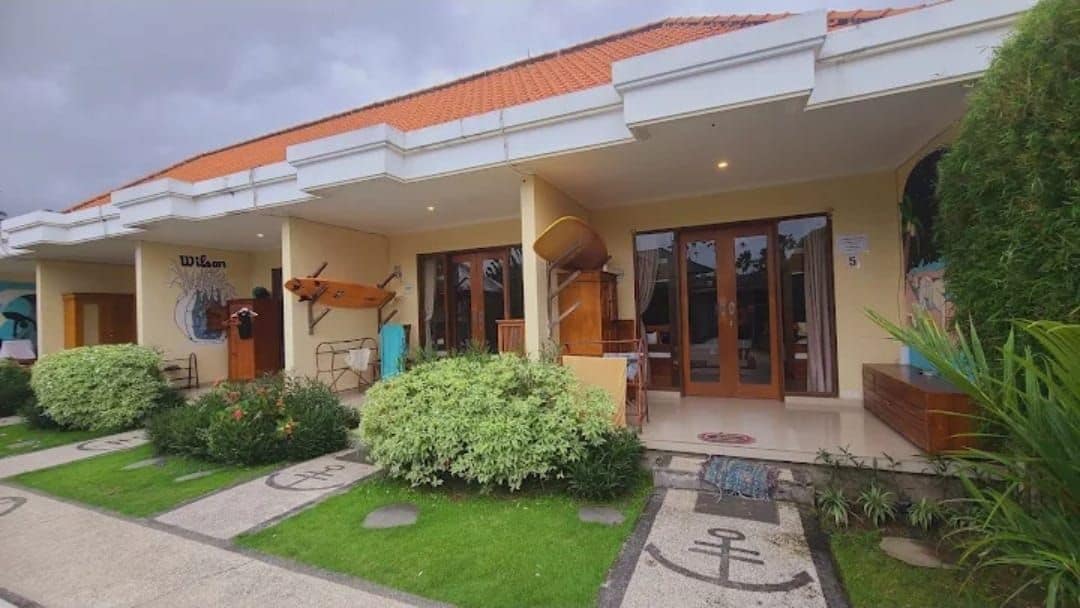 A hotel with a covered entrance, a signboard, and a well-maintained garden area.