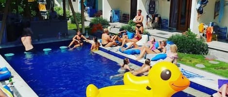 Zona de piscina con juguetes inflables y gente relajándose.