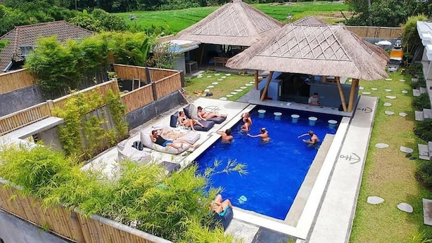 A swimming pool area with lounge chairs and a thatched-roof structure. - Castaway Hostel (Badung)
