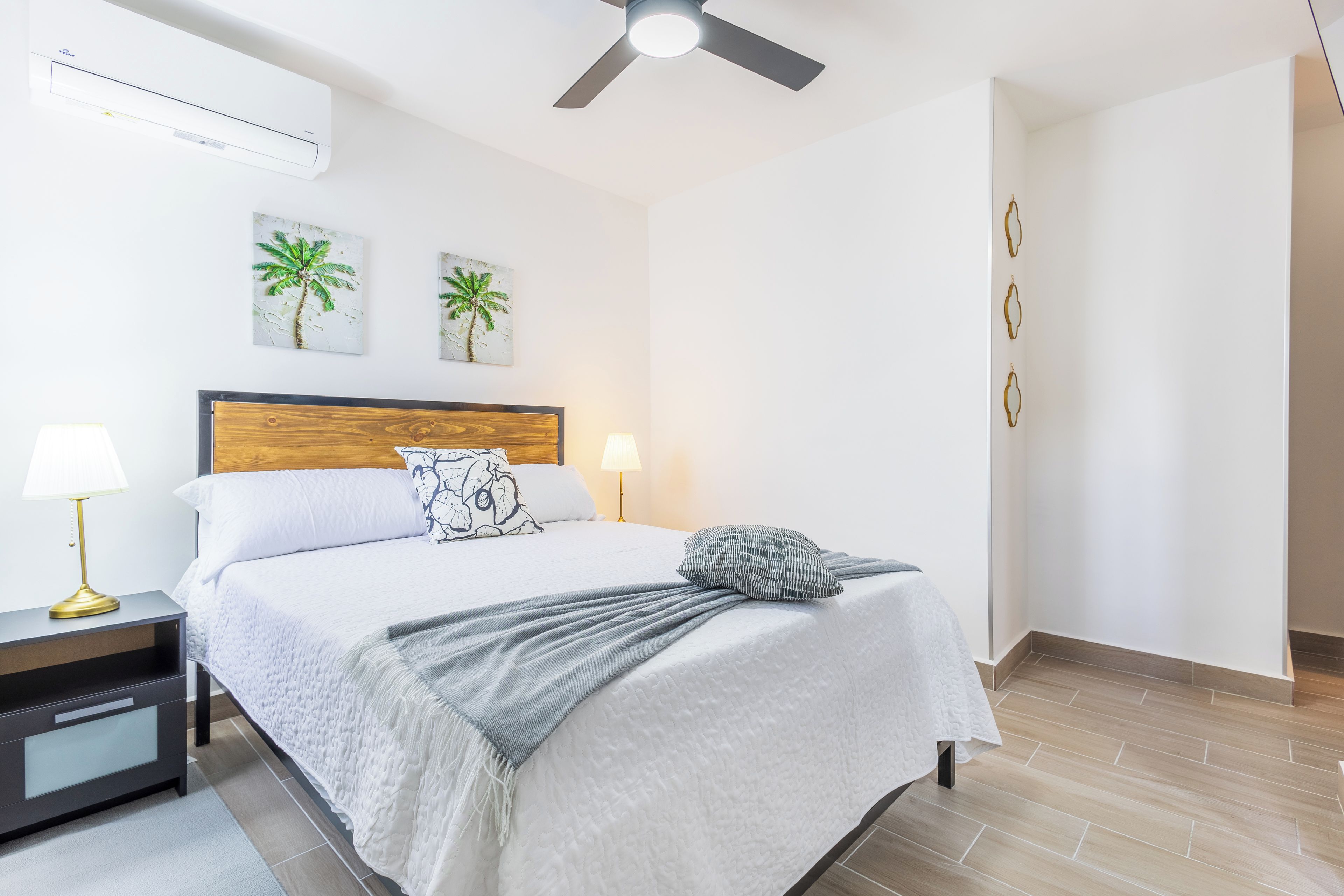 Ein Hotelzimmer mit einem Bett, Nachttischlampen, einem Deckenventilator und zwei Wandklimaanlagen.