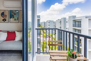 Ein Balkon mit einer hölzernen Bank, einem Blumentopf und Blick auf eine Wohngegend mit mehreren Gebäuden.