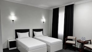 A hotel room with two single beds, a chair, a small table with water bottles, and a nightstand. - Reikartz Termez Palace (Farg'ona)