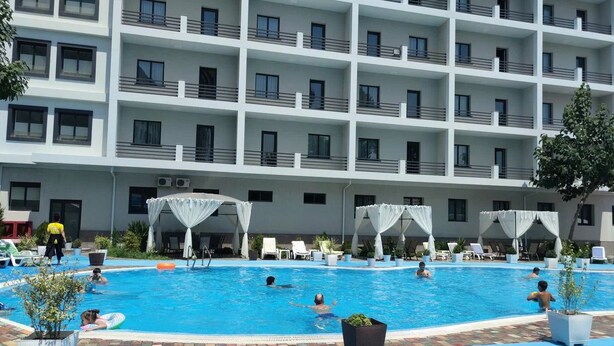 A hotel pool area with multiple levels of balconies, lounge chairs, and umbrellas. - Reikartz Termez Palace (Farg'ona)