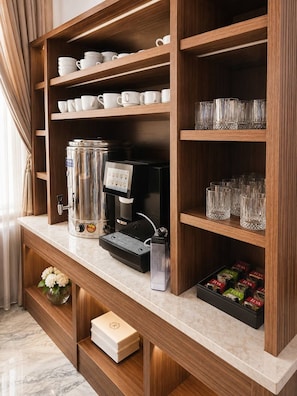 Una zona de cafè amb una màquina de cafè, tasses i un plat de càpsules de cafè.