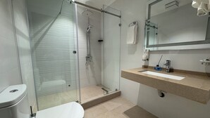 A bathroom with a glass-enclosed shower, a white toilet, a sink with a mirror above it, and a towel hanging on the wall. - Reikartz Termez Palace (Farg'ona)