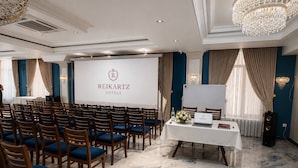 A conference room with rows of chairs, a presentation screen, and a table with a laptop and flowers. - Reikartz Termez Palace (Farg'ona)