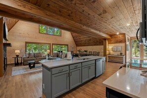 A spacious kitchen with a large island, wooden ceiling, and a cozy seating area with a sofa and chairs. - Brand new three bedroom three bathroom A-Frame Cabin (Sevierville)