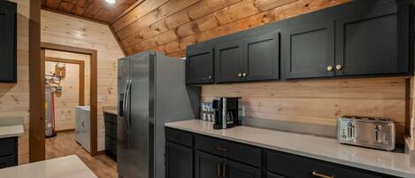 A kitchen with dark cabinets, a stainless steel refrigerator, a toaster, and a coffee maker.