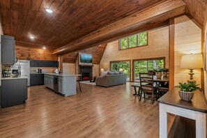 Un intérieur spacieux comprenant une cuisine, un coin repas et un salon, avec un plancher en bois et un plafond haut.