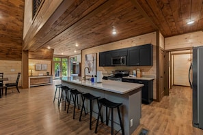 A modern kitchen with a central island, bar stools, and dark cabinetry. - Brand new three bedroom three bathroom A-Frame Cabin (Sevierville)
