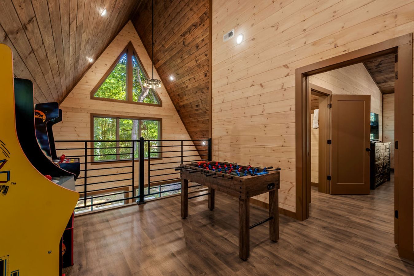 A wooden interior with a foosball table, a window with a view of trees, and a door leading to another room.