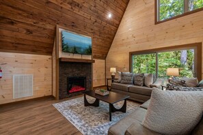 Un salon chaleureux avec une cheminée, un canapé, une table basse et une grande fenêtre donnant sur l’extérieur.