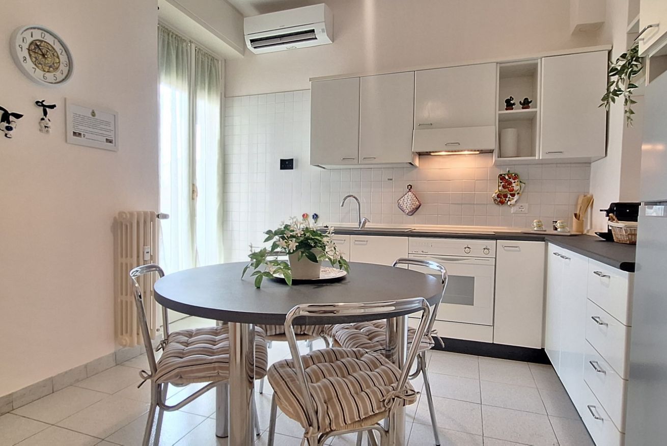 Una cocina moderna con armarios blancos, una mesa de comedor redonda con sillas a rayas y una planta en maceta sobre la mesa.