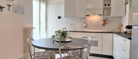 Una cocina moderna con armarios blancos, una mesa de comedor redonda con sillas a rayas y una planta en maceta sobre la mesa.