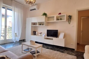A modern living room with a sofa, a coffee table, a flat-screen TV, and built-in shelving. - Il Nido di Artemisia - Relaxing Florentine home (Florence)