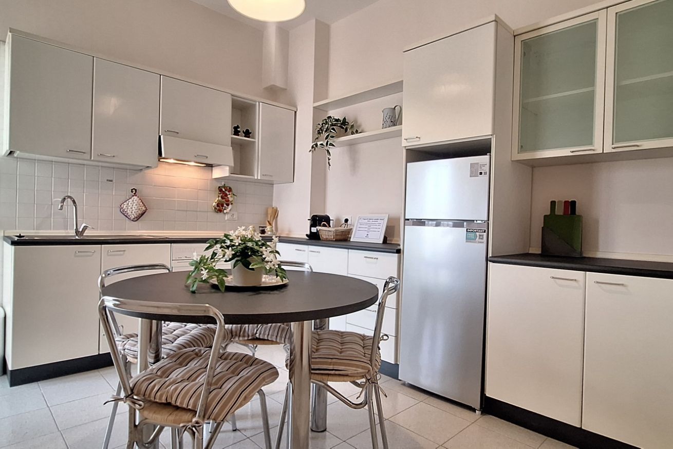 Une cuisine moderne avec des meubles blancs, un réfrigérateur en acier inoxydable et une table à manger avec des chaises.