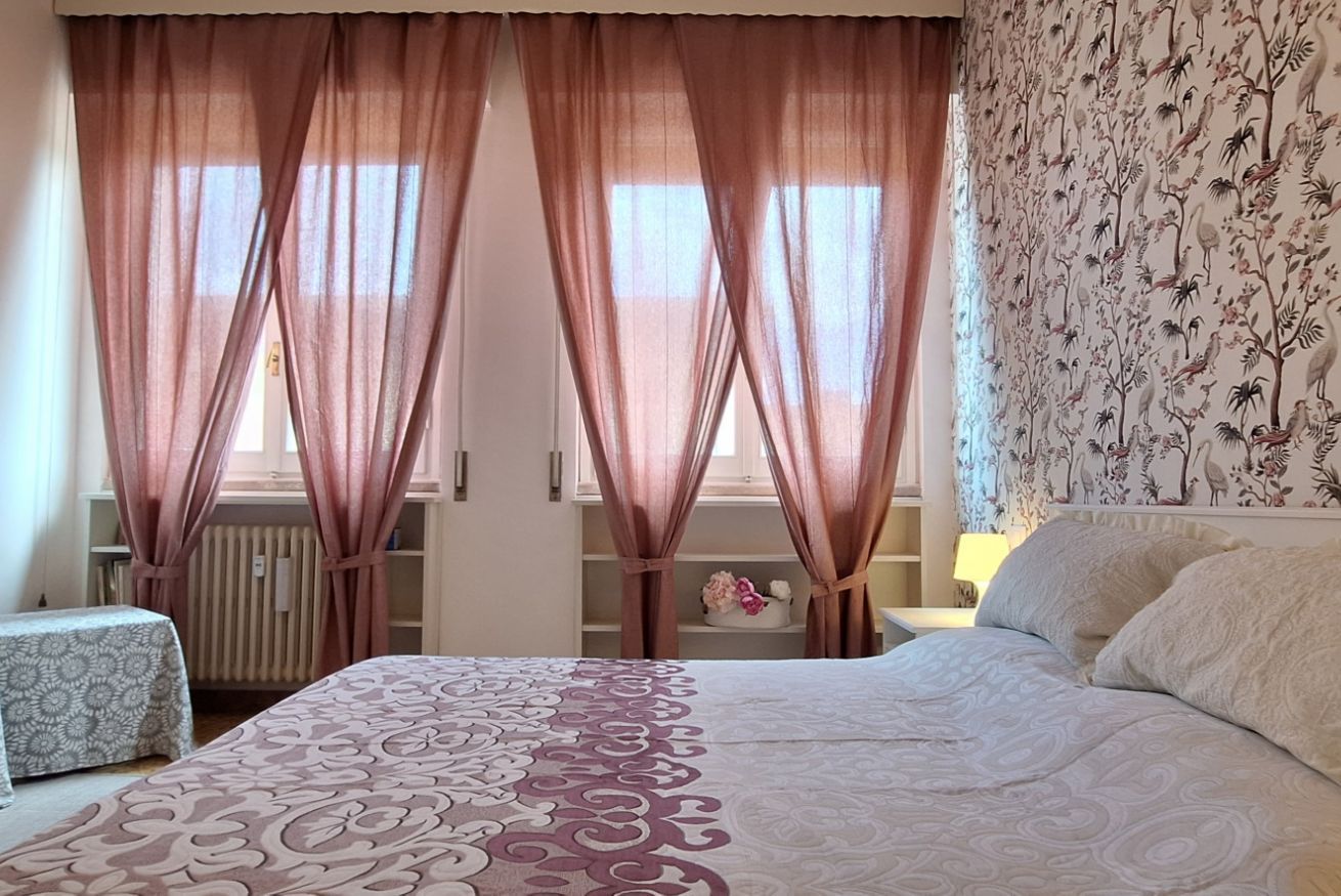 Une chambre à coucher avec un grand lit, une table de chevet, une commode et une fenêtre avec des rideaux.