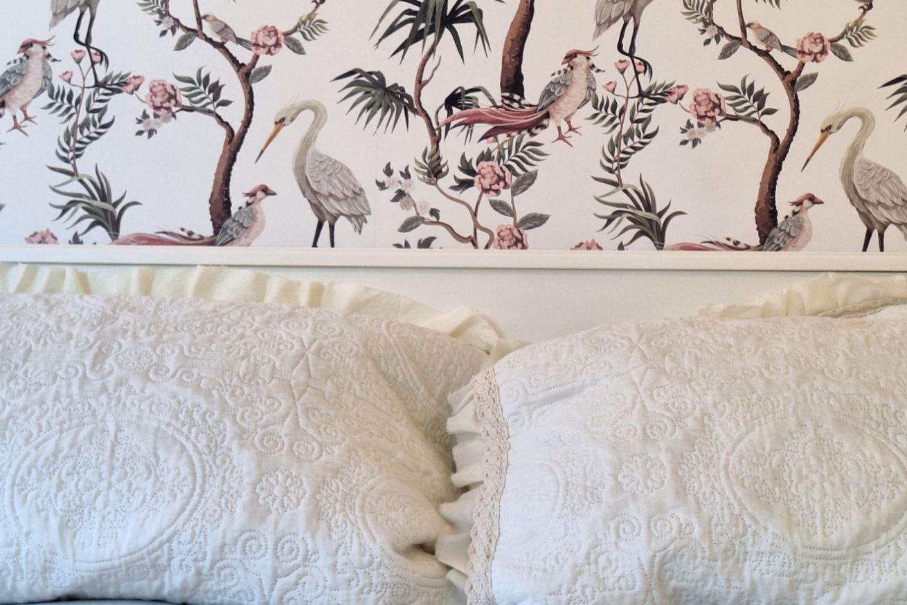 Ein Schlafzimmer mit floraler Tapete und zwei Kissen mit Strukturmuster.