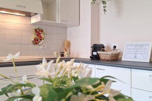 A kitchen with white cabinets, a white tiled backsplash, a hanging kitchen towel, a coffee maker, and a basket on the counter. - Il Nido di Artemisia - Relaxing Florentine home (Florence)
