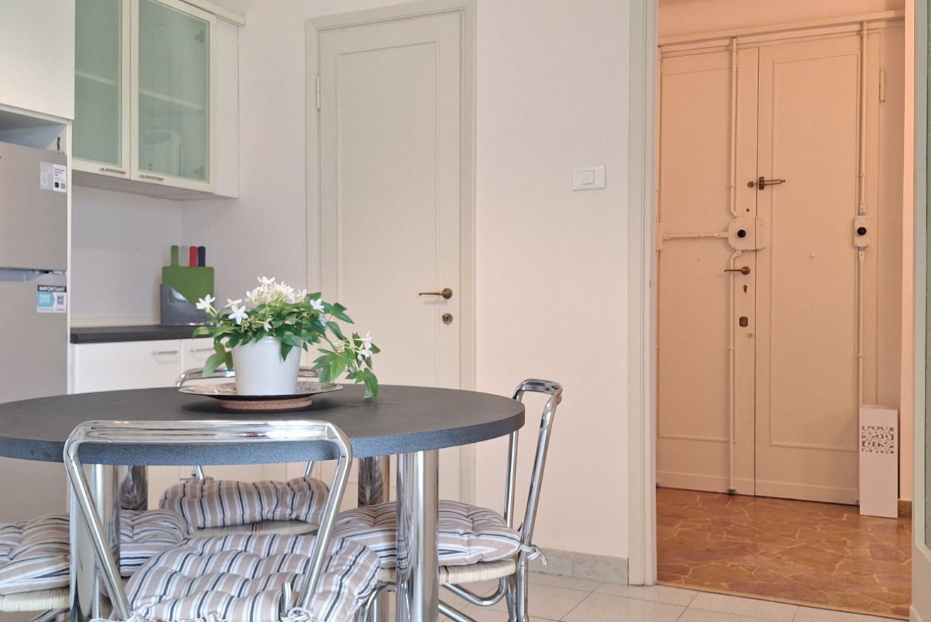 Un coin repas avec une table ronde, des chaises à coussins rayés, une plante en pot et une porte blanche avec une serrure.
