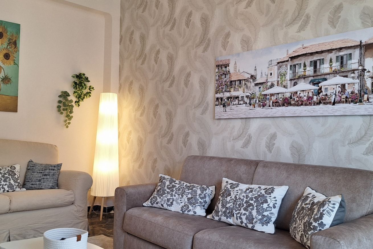 Een woonkamer met een bank, kussens, een lamp, een schilderij en behang met een patroon.