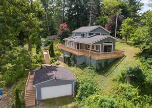 A two-story house with a deck, surrounded by dense greenery.