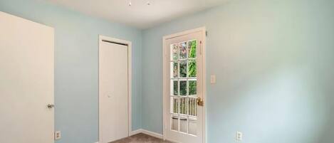 A room with a ceiling fan, a door, and a window with a view of greenery.
