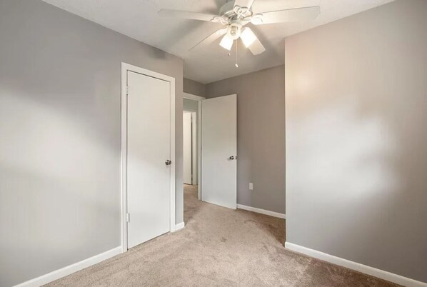 A hallway with carpeted floors, white walls, and a ceiling fan.