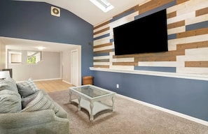 Ein Wohnzimmer mit blauer Wand, einem Wand-Fernseher, einem Glastisch und einem grauen Sofa.
