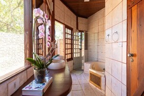 A bathroom with a bathtub, a sink, and a window with plants. - Pousada Fazenda São Bento (Alto Paraíso de Goiás)