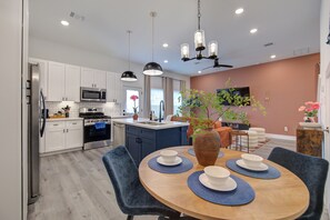 A modern kitchen with white cabinets, a microwave, and a stove. There is a dining area with a wooden table and blue chairs. - Gated 3BR Home, Garage + Fenced Backyard, 15 Min to Galleria & Downtown (Houston)