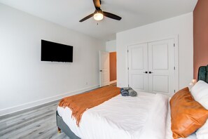 A bedroom with a bed, a ceiling fan, a TV mounted on the wall, and a door leading to another room. - Gated 3BR Home, Garage + Fenced Backyard, 15 Min to Galleria & Downtown (Houston)