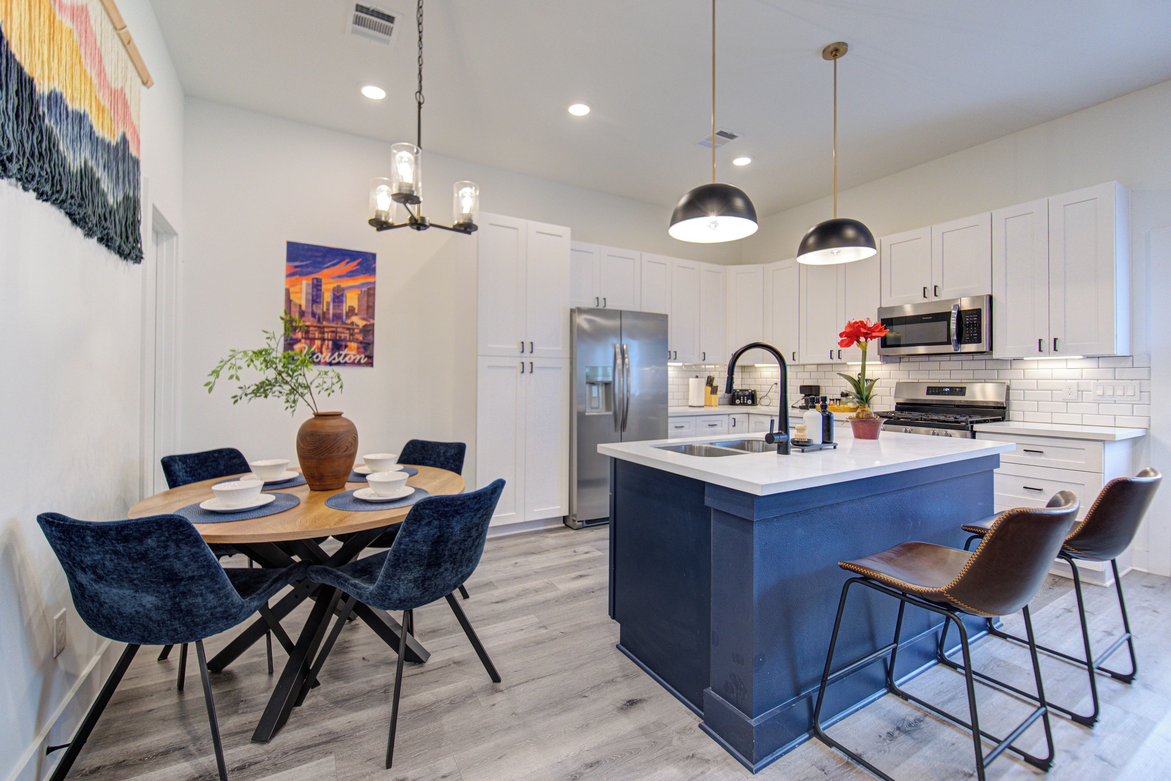A modern kitchen with white cabinets, a central island with bar stools, and a dining area with blue chairs.
