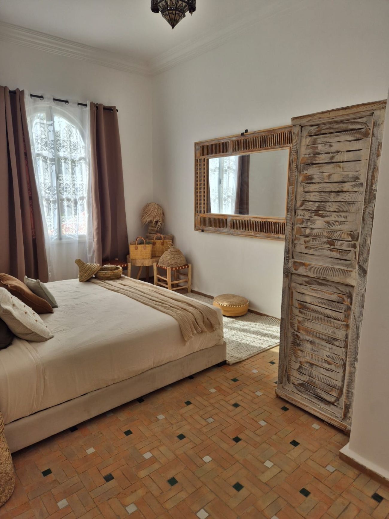 Een slaapkamer met een bed, een spiegel, een kledingkast en een raam met gordijnen.