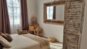 A bedroom with a bed, a mirror, a wardrobe, and a window with curtains. - Villa Dar Serenity (Ounara)