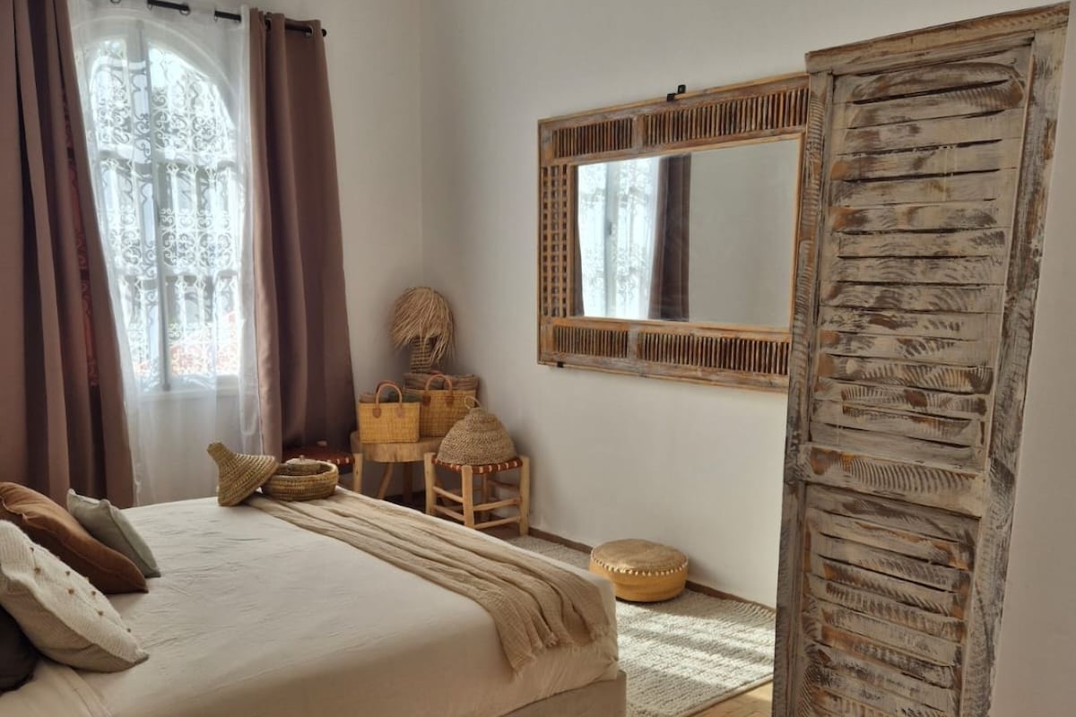 Quarto com cama, espelho, guarda-roupa e janela com cortinas.