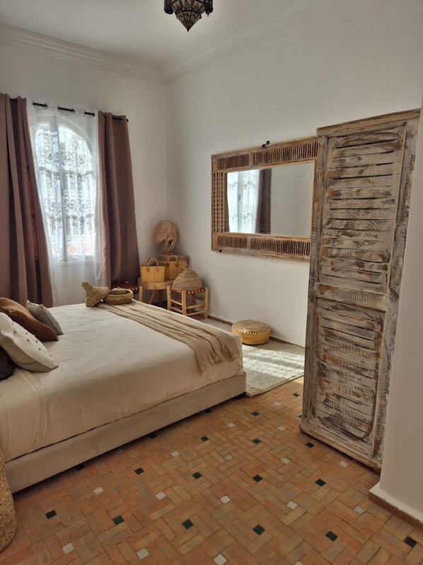 A bedroom with a bed, a mirror, a wardrobe, and a window with curtains.
