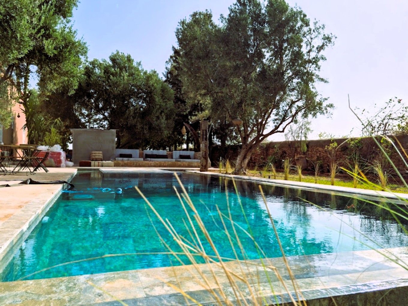 A rectangular swimming pool with clear blue water, surrounded by a stone deck and a grassy area with trees.