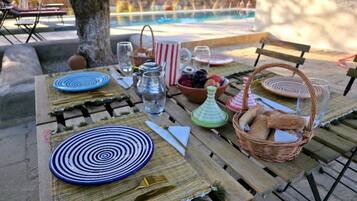 An outdoor dining table set with plates, cutlery, glasses, and a basket of bread.