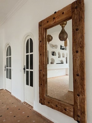 A hallway with white walls, a wooden-framed mirror, and two arched doorways.