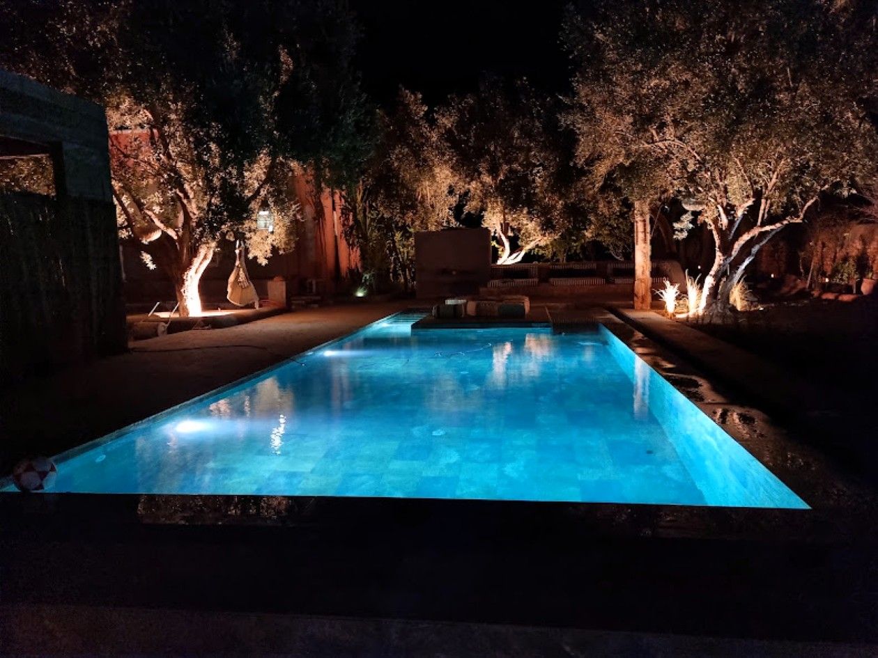 Una piscina rectangular de noche, rodeada de árboles y una estructura de piedra.