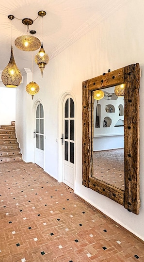 A hallway with patterned flooring, a wooden-framed mirror, and hanging lamps.