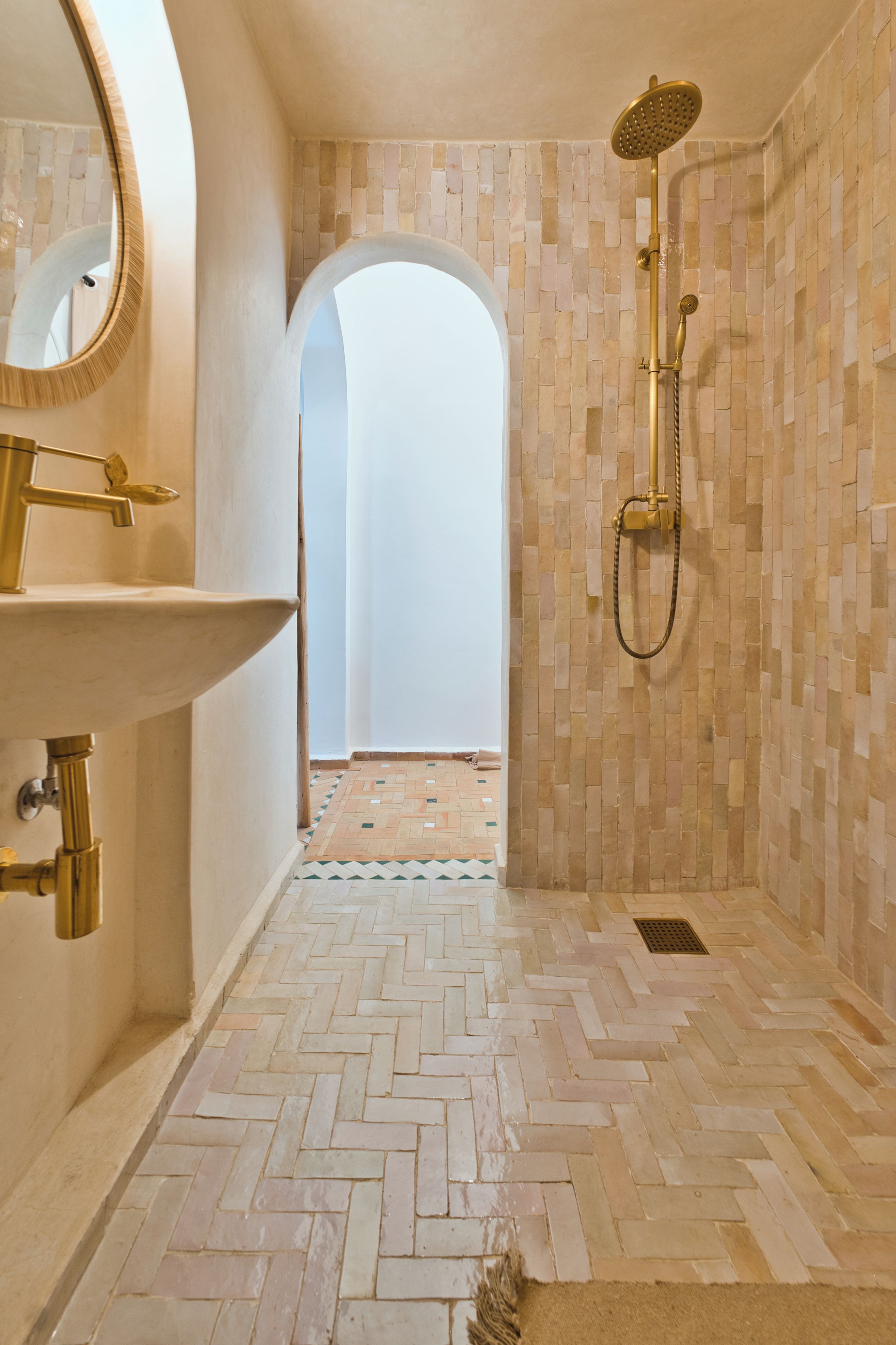 Un baño con piso de espiga, grifo dorado, ducha y espejo.