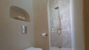 A bathroom with a freestanding toilet, a shower area with a tiled wall, and a small rug on the floor.
