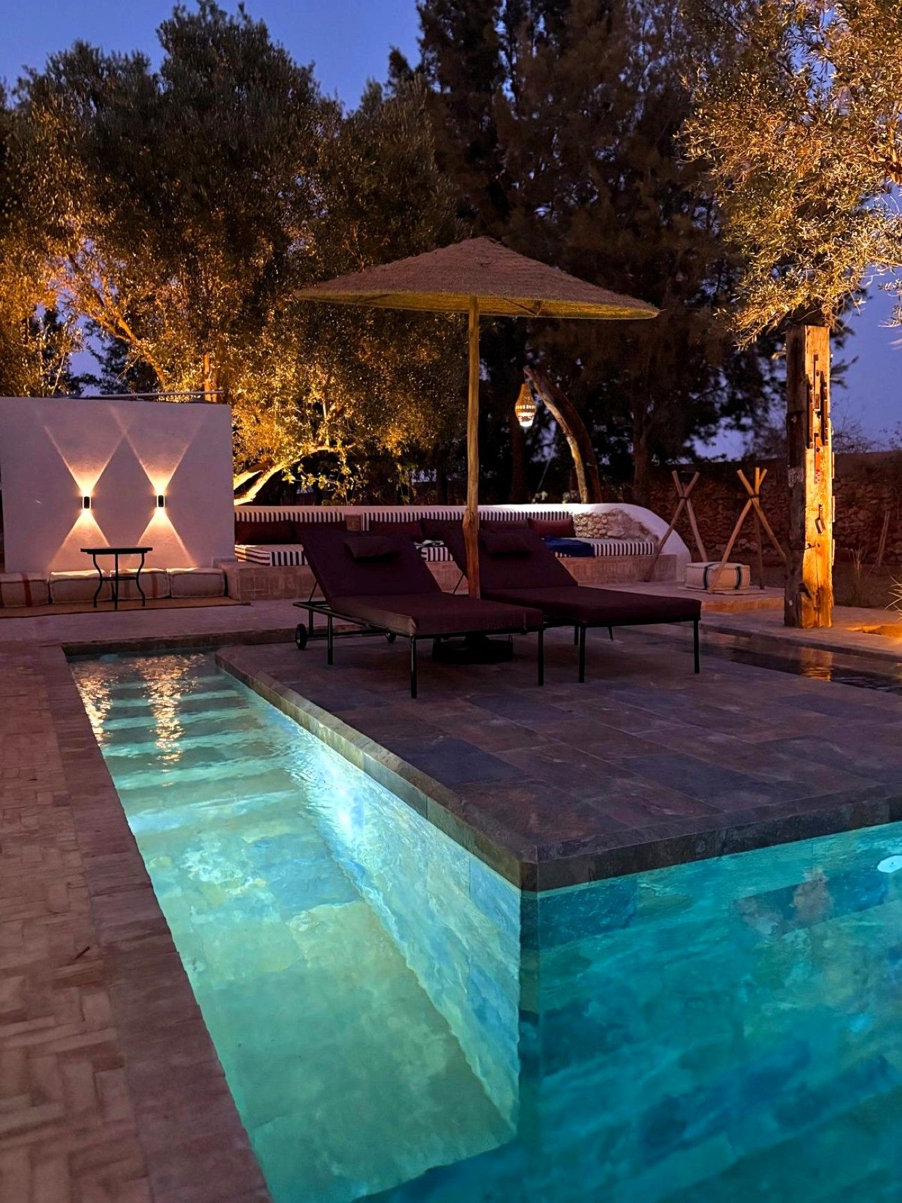 A swimming pool with lounge chairs and a pergola, surrounded by trees and a stone wall.