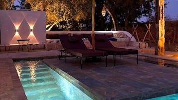 A swimming pool with lounge chairs and a pergola, surrounded by trees and a stone wall.